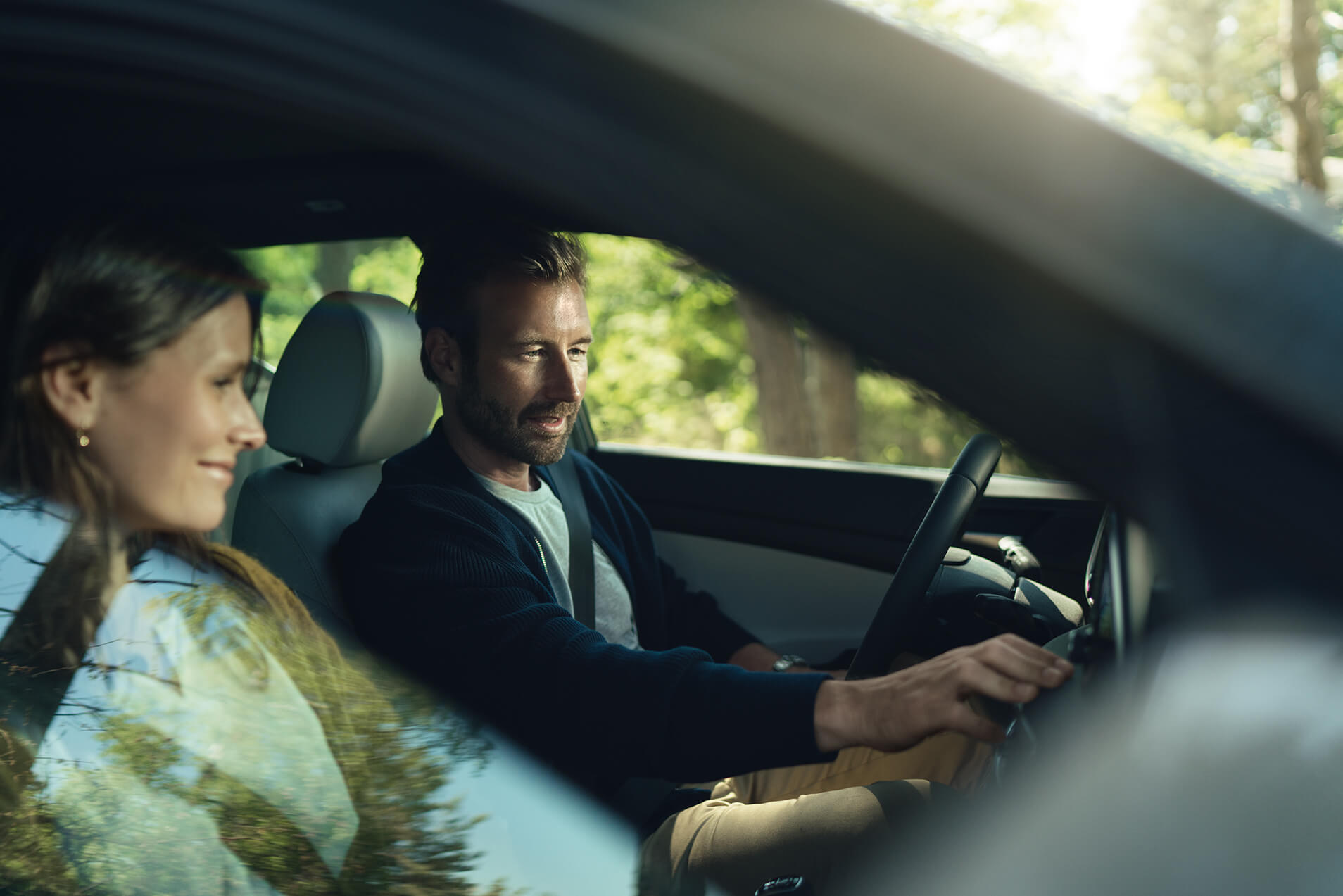 Pareja sonriente viajando mientras regulan los controles de un coche eléctrico 